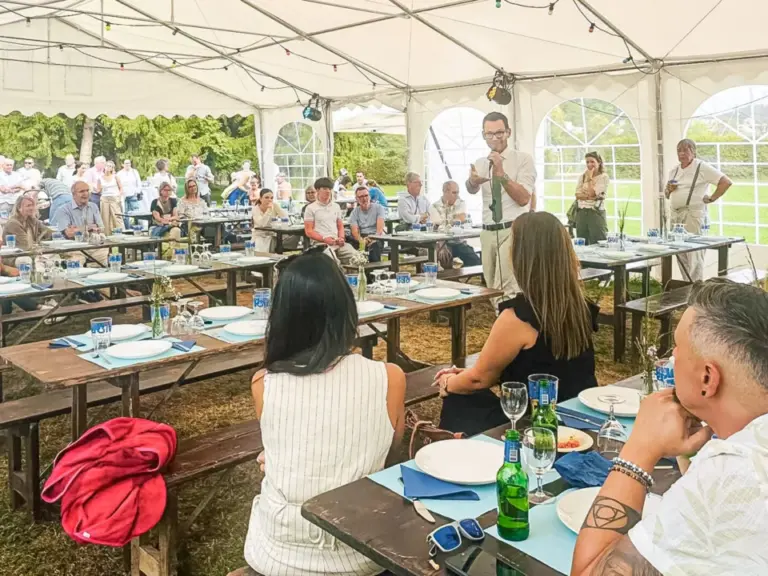 In einem Festzelt sitzen Menschen an Biertischen, während ein Mann vorne mit Mikrofon spricht.