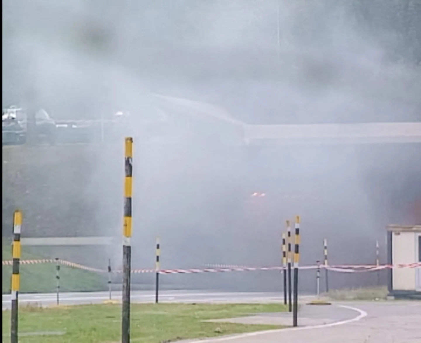 Dichter Rauch verhüllt eine Absperrung mit Flatterband und gestreiften Pfosten vor einem Gebäude.