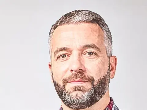 Ein bärtiger Mann mit verschränkten Armen in kariertem Hemd blickt in die Kamera.