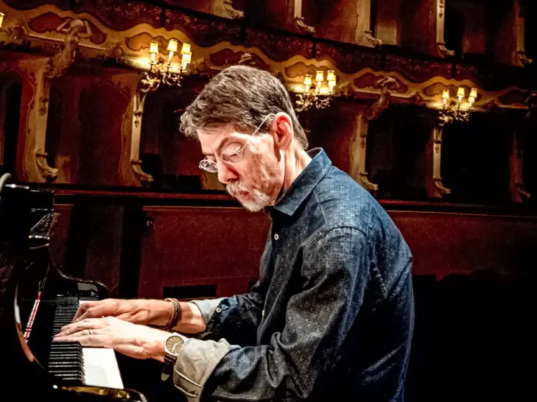 Ein älterer Mann mit Brille und Bart spielt konzentriert Klavier in einem historischen Theatersaal.