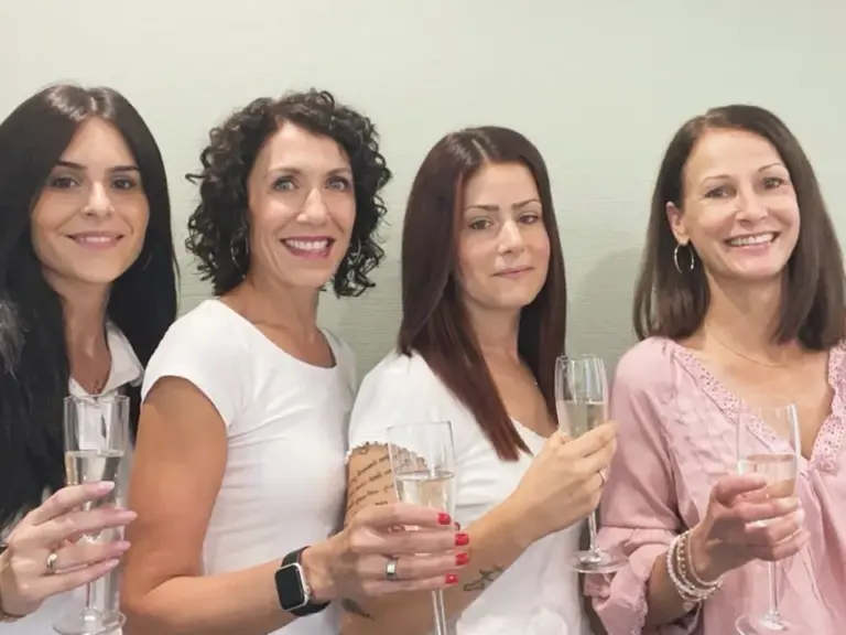 Vier lächelnde Frauen stossen mit Sektgläsern an und blicken in die Kamera.