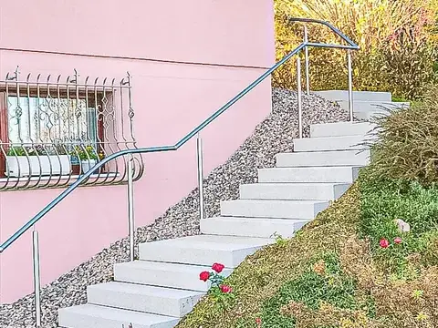 Steintreppe mit geschwungenem Metallhandlauf führt an einem rosa Haus vorbei durch einen Garten.