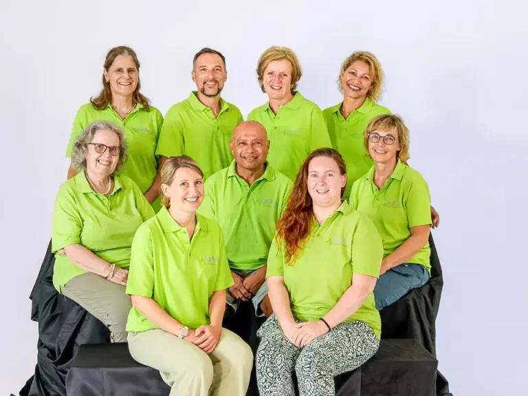 Gruppe von neun Personen in grünen Poloshirts posiert lächelnd für ein Gruppenfoto vor hellem Hintergrund.