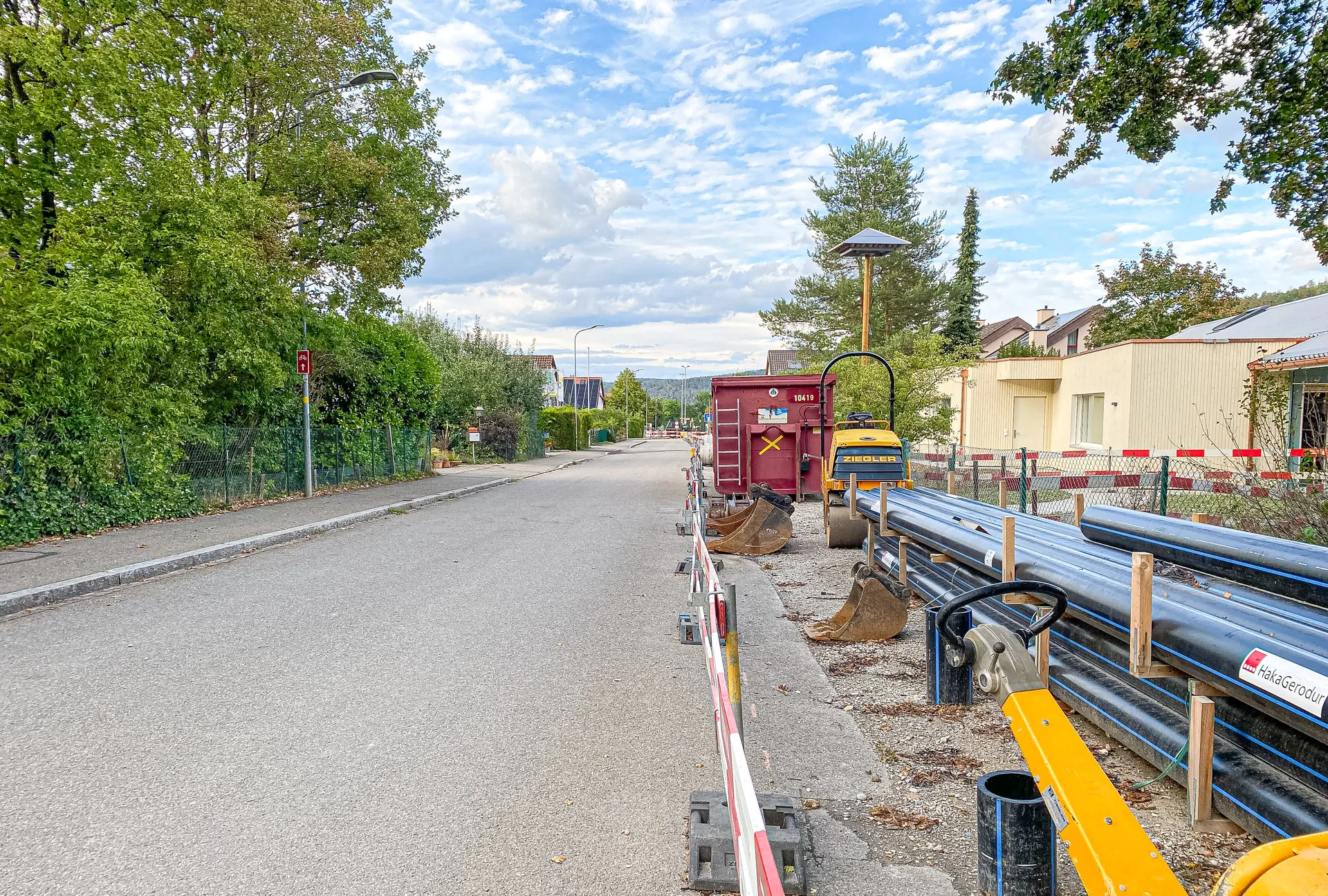 Baustelle an einer Strasse mit Container, Rohren und Absperrungen am Fahrbahnrand.