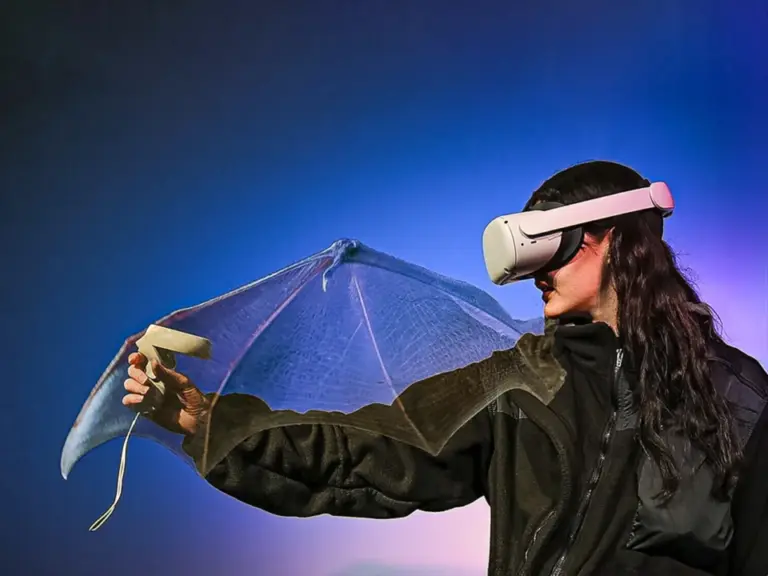 Eine Person mit VR-Brille streckt einen Arm mit fledermausflügelartiger Konstruktion aus.