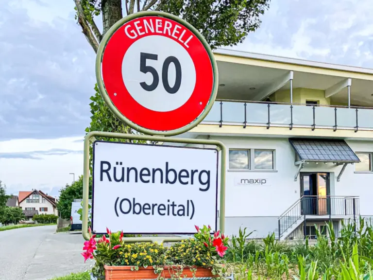 Ortstafel «Rünenberg (Obereital)» mit Tempo-50-Schild, darunter Blumenkasten, im Hintergrund ein Gebäude.