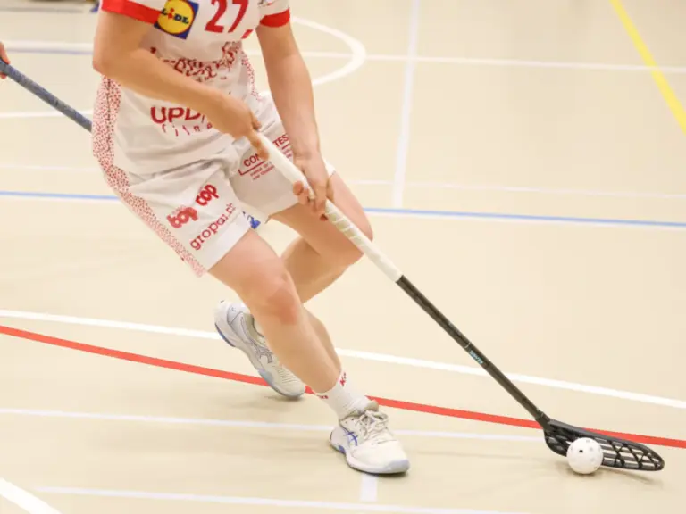 Zwei Unihockeyspielerinnen mit Schlägern kämpfen in der Halle um den Ball.