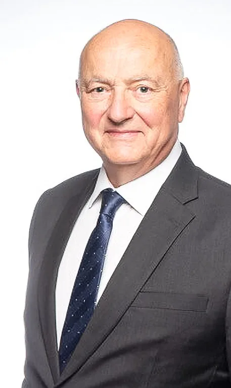 Ein älterer Mann mit Glatze im dunklen Anzug und gepunkteter Krawatte blickt lächelnd in die Kamera.