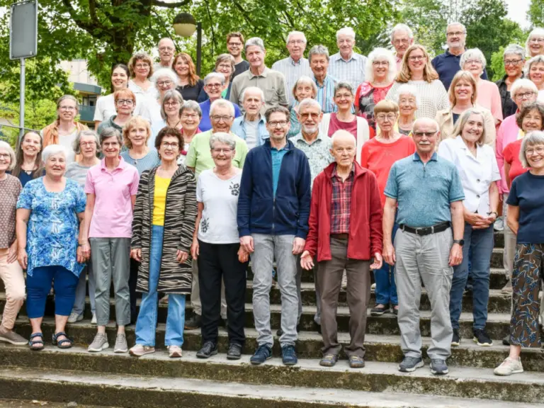 Eine grosse Gruppe von Chormitgliedern unterschiedlichen Alters steht und sitzt für ein Gruppenfoto auf einer Freilufttreppe.