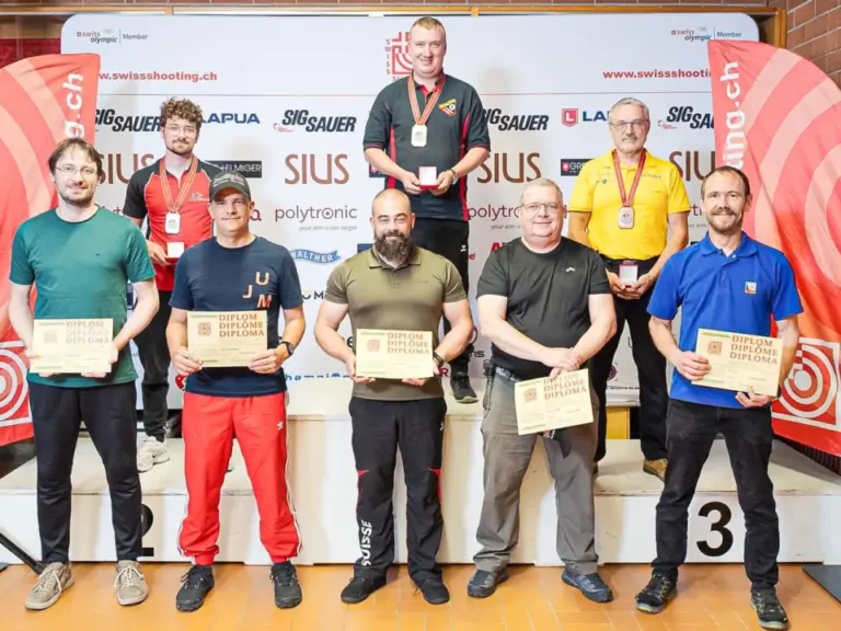 Sieben Männer mit Diplomen und Medaillen stehen für ein Gruppenfoto vor einer Sponsorenwand.