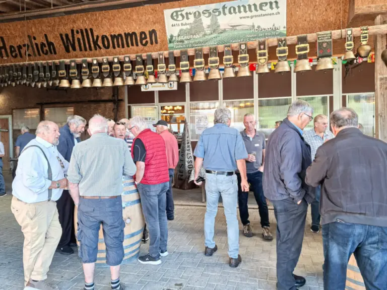Mehrere ältere Männer stehen im Gespräch in einer Halle mit Kuhglocken an der Wand.