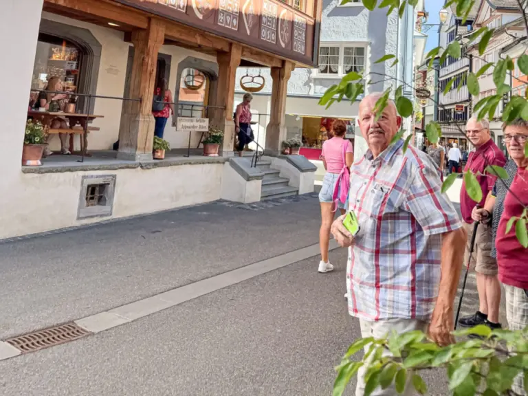 Mehrere ältere Menschen stehen vor einem bemalten Fassadenhaus in einer Altstadtgasse.