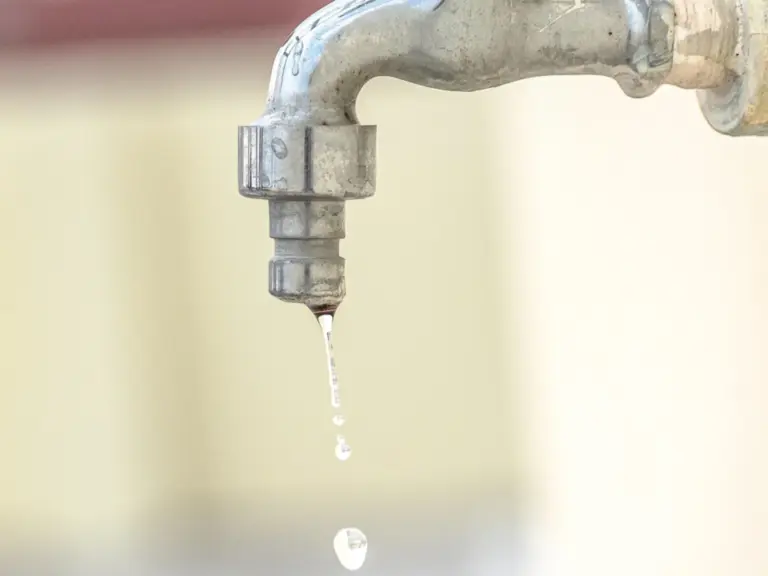 Aus einem metallischen Wasserhahn tropft langsam Wasser vor unscharfem Hintergrund.
