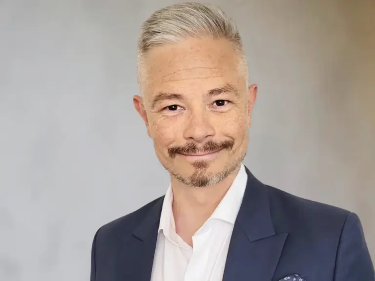 Ein Mann mit grauem Kurzhaar und Bart im dunkelblauen Anzug lächelt in die Kamera.