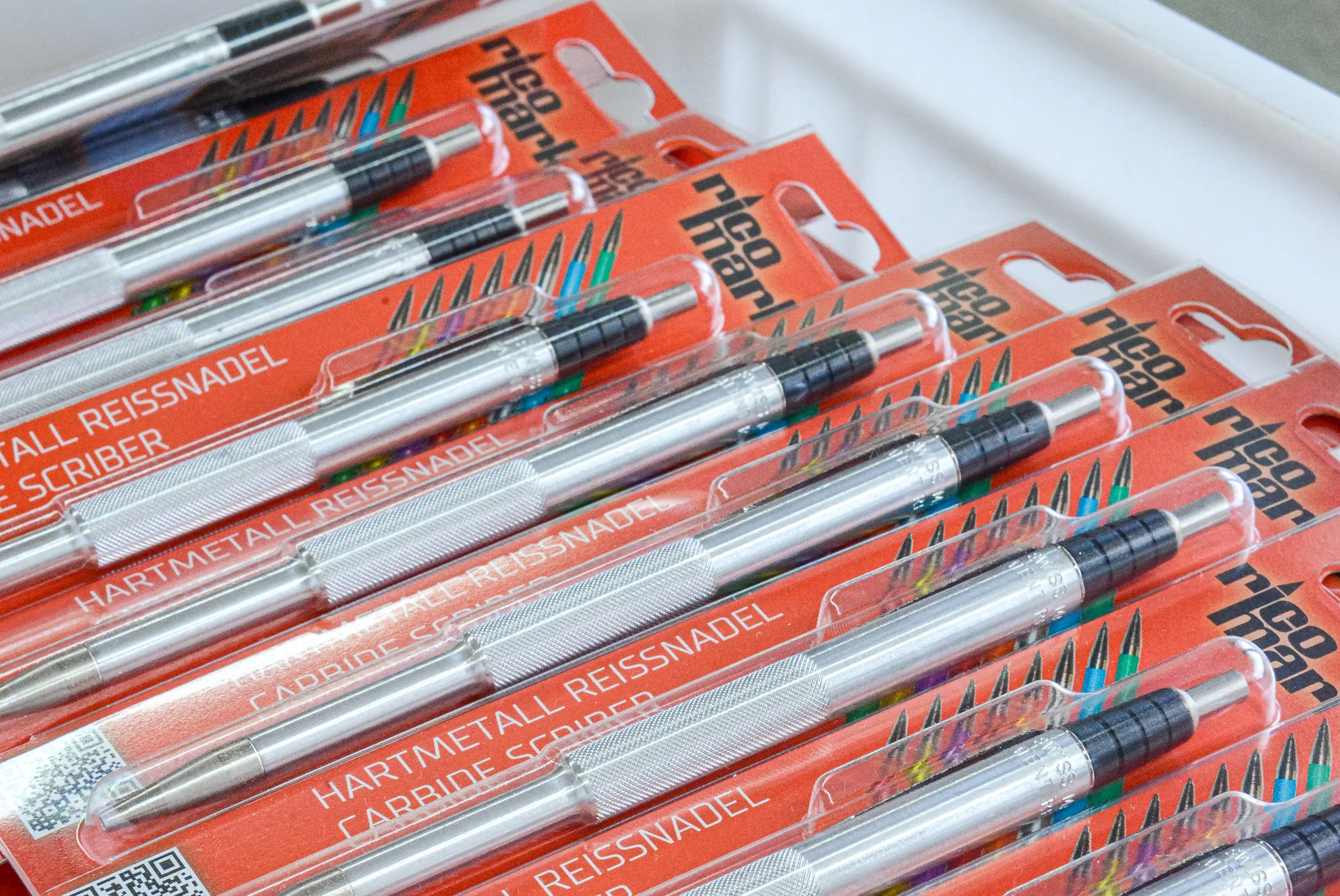 Mehrere verpackte Hartmetall-Reissnadeln (Carbide Scriber) liegen gestapelt in einer weissen Kunststoffkiste.