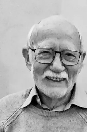 Ein lächelnder älterer Mann mit Brille und weißem Bart trägt einen Pullover.