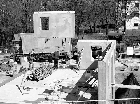 Bauarbeiter richten grosse Betonfertigteile auf einer Baustelle mit Kran und Lastwagen auf.