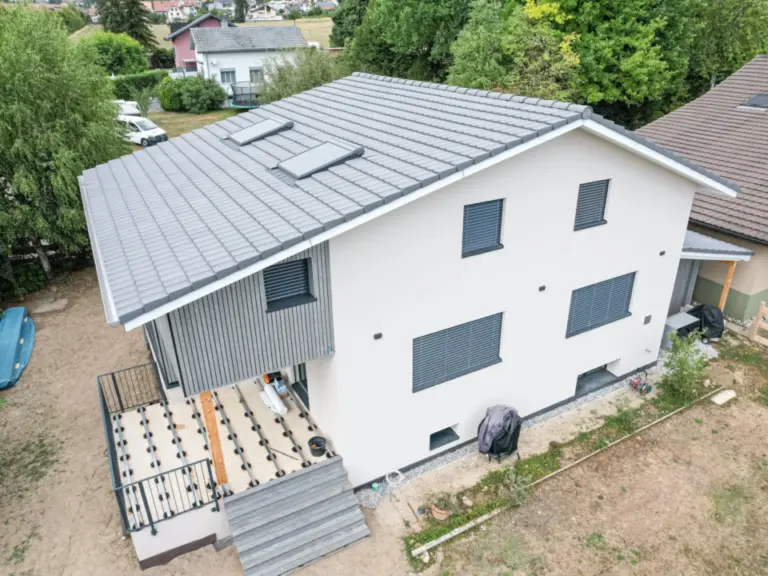 Luftaufnahme eines neu gebauten weissen Einfamilienhauses mit grauem Ziegeldach und Holzterrasse im Bau.