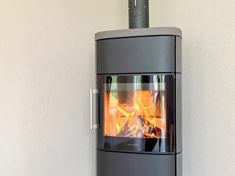 Ein moderner schwarzer Kaminofen mit brennendem Feuer steht in einer Zimmerecke.