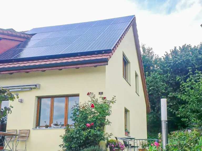 Gelbes Einfamilienhaus mit Solaranlage auf dem Dach und blühendem Garten davor
