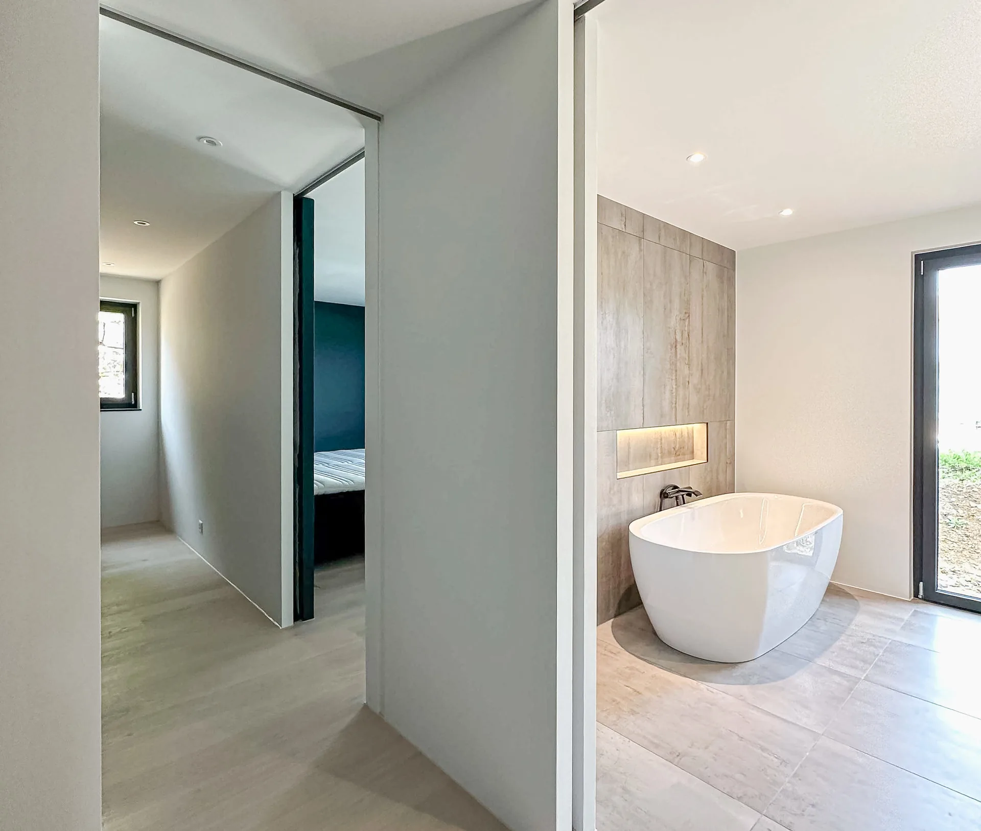 Modernes Badezimmer mit freistehender ovaler Badewanne, Fliesenwand und Blick ins Freie
