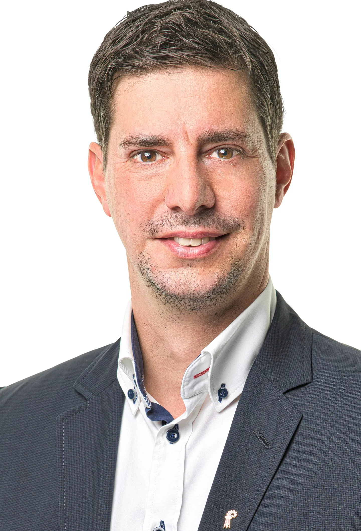 Ein lächelnder Mann mit kurzen dunklen Haaren, Anzug und weissem Hemd blickt in die Kamera.