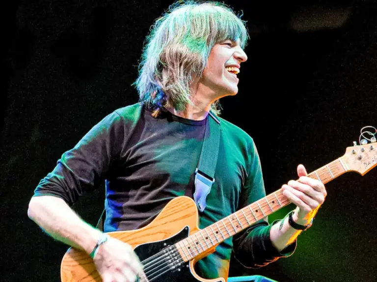 Ein lachender Gitarrist mit langen grauen Haaren spielt auf der Bühne eine E-Gitarre.