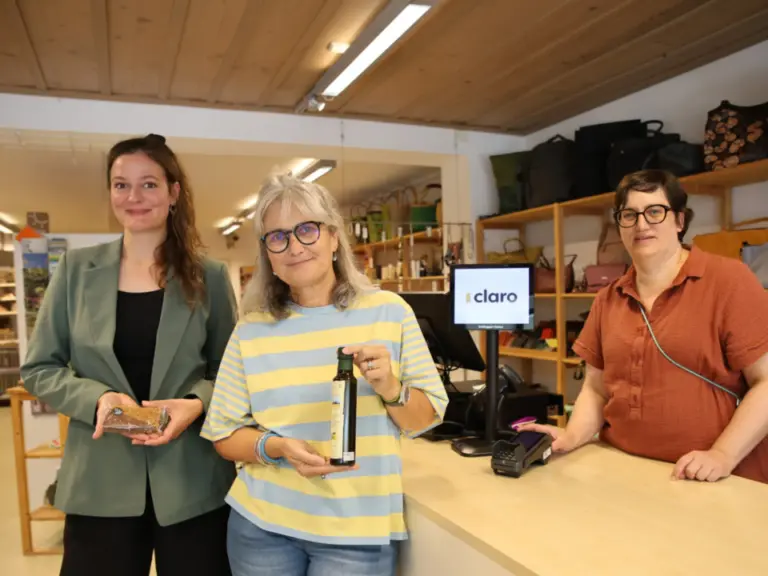 Drei Frauen stehen lächelnd an einer Ladentheke, zwei halten Produkte in den Händen.