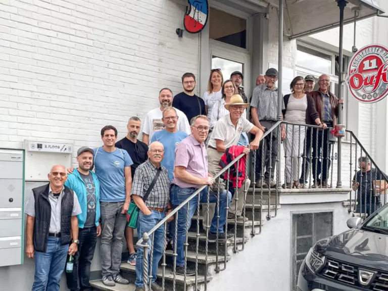 Eine Gruppe von etwa zwanzig Personen steht und posiert auf einer Aussentreppe vor einem weissen Gebäude.
