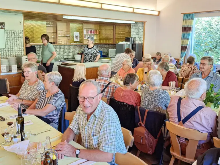 Menschen sitzen an gedeckten Tischen in einem Speisesaal und unterhalten sich beim Essen.