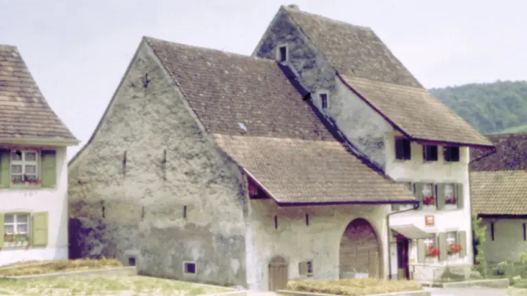 Altes verputztes Bauernhaus mit grossem Satteldach und Rundbogentor im Dorf.