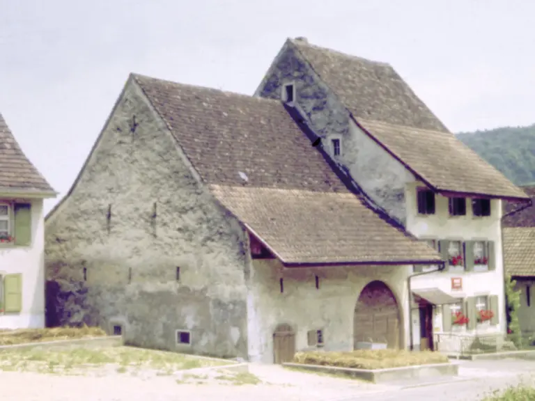 Altes verputztes Bauernhaus mit grossem Satteldach und Rundbogentor im Dorf.